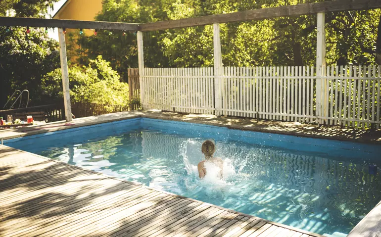 Ett barn hoppar ner i en pool med ett stort plask, runt polen finns ett staket