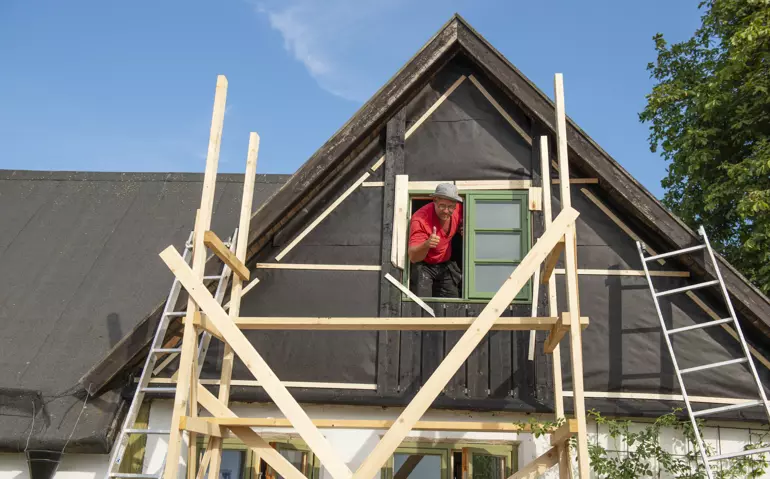 Takkupa med ett fönster som byggs om, byggställningar står runt takkupan, i fönstret sitter en man i röd tröja