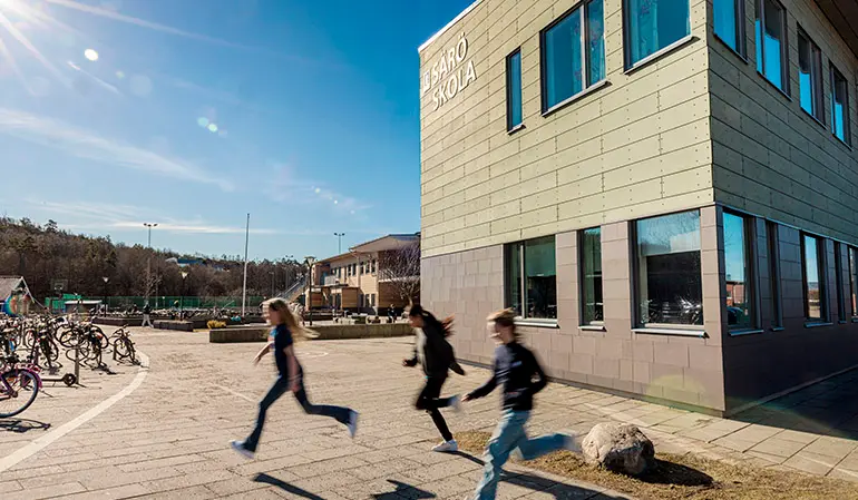 Säröskolans ljusbruna byggnad. På byggnaden står det Särö skola. Framför byggnaden springer tre elever. I bakgrunden skymtar en skolgård med fotbollsplan.