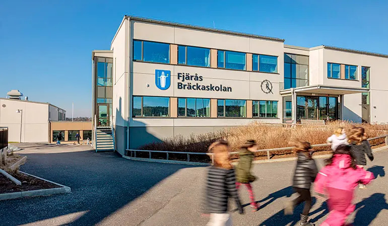 I bakgrunden syns Fjärås Bräckaskolans ljusbruna skolbyggnad. Flera elever syns springa framför byggnaden.
