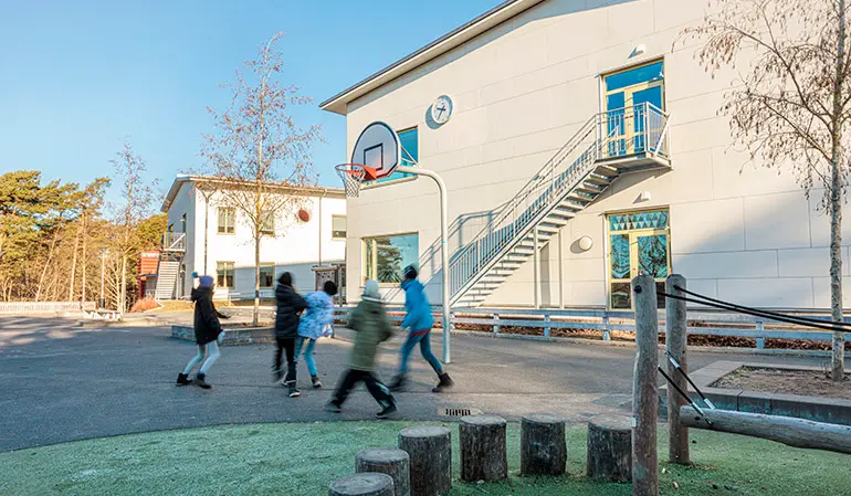Furulidsskolan vita byggnad. Framför byggnaden spelar flera elever basket.