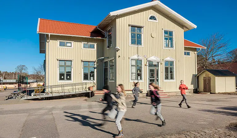 Iseråsskolans ljusbruna byggnad. Framför byggnaden springer flera elever.