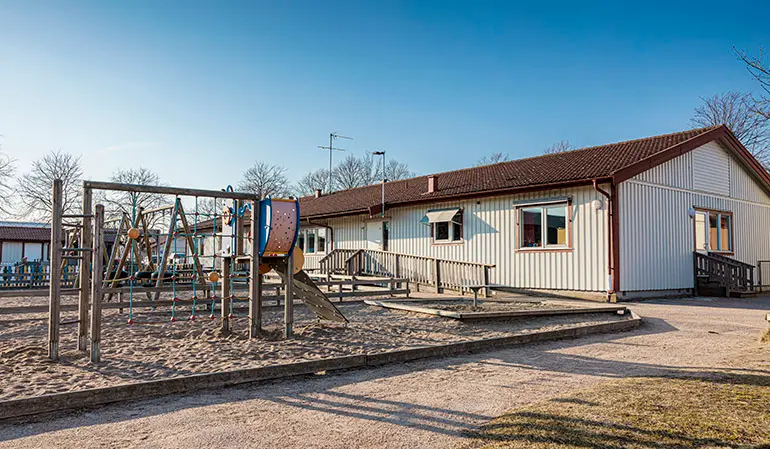 Klinnekärrs förskolas vita byggnad. Framför byggnaden syns förskolans gård med klätterställningar och gungor.
