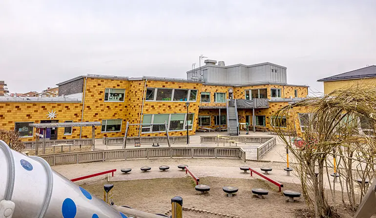 Varlaförskolas gula byggnad. Framför byggnaden finns en gård med balanshinder. 