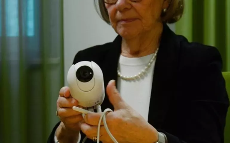 En äldre kvinna håller i en trygghetskamera.