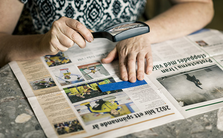 En hand som håller ett förstoringsglas över en tidning.