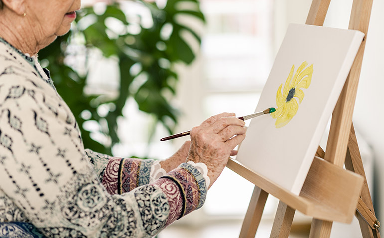 En äldre kvinna målar en tavla.