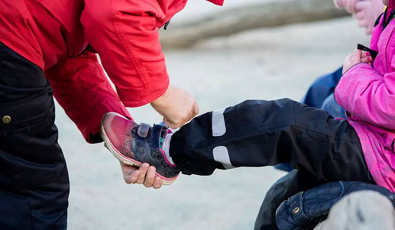 Pedagog hjälper ett barn med skorna.