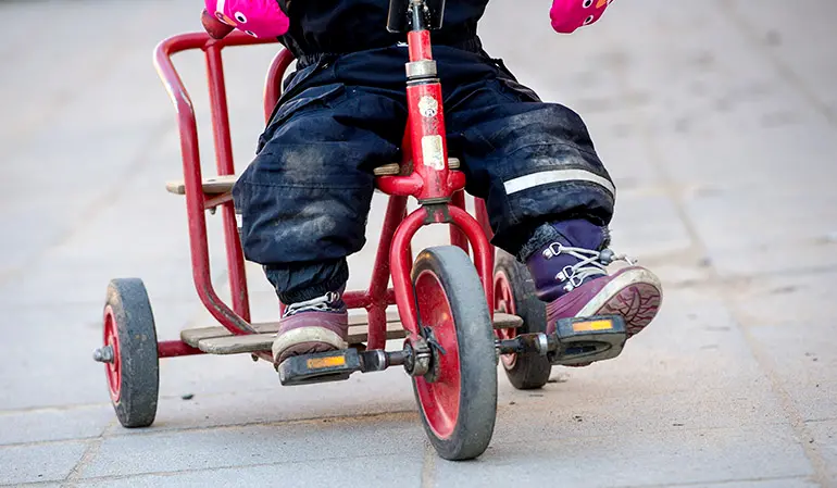 Ett barn cyklar på en röd cykel.