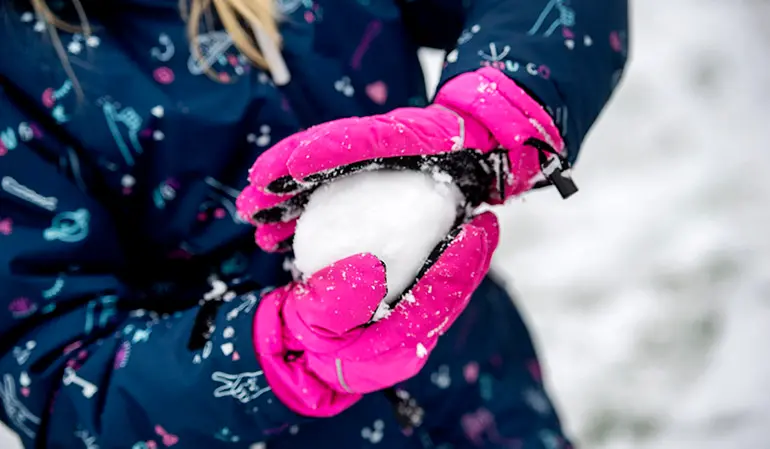 Elev med rosa vantar kramar en snöboll.