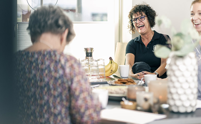 En kvinna sitter vid ett bord och skrattar tillsammans med andra. 