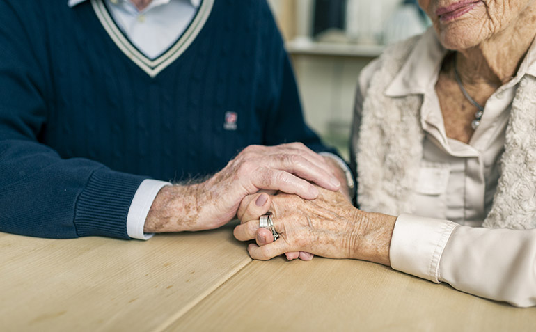 Två äldre personer som håller varandra i handen.
