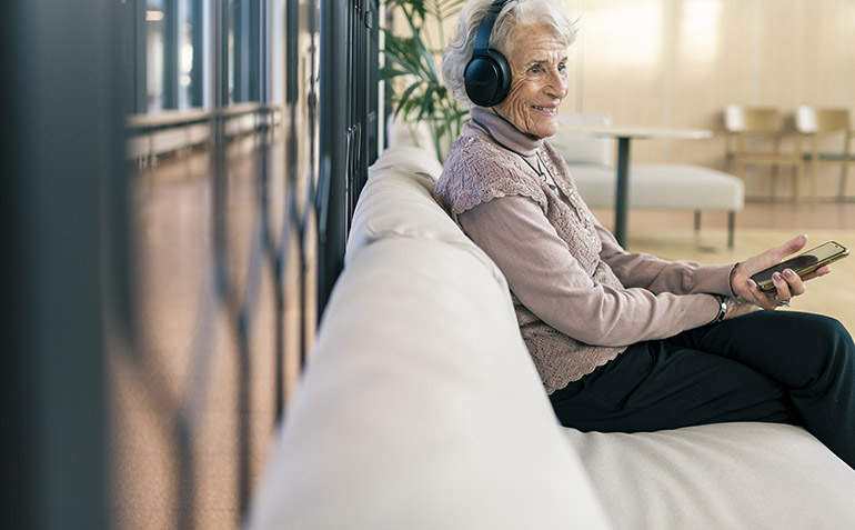 En äldre kvinna sitter i en soffa och lyssnar på musik.