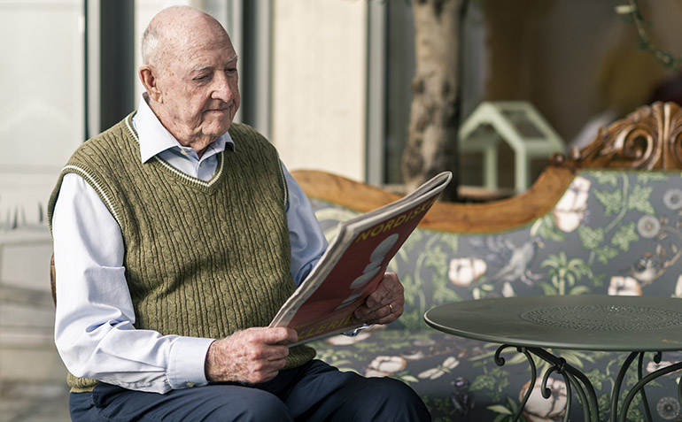 En äldre man sitter och läser en tidning.