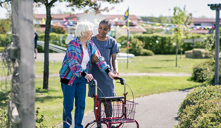 En äldre kvinna med rullator tillsammans med en undersköterska