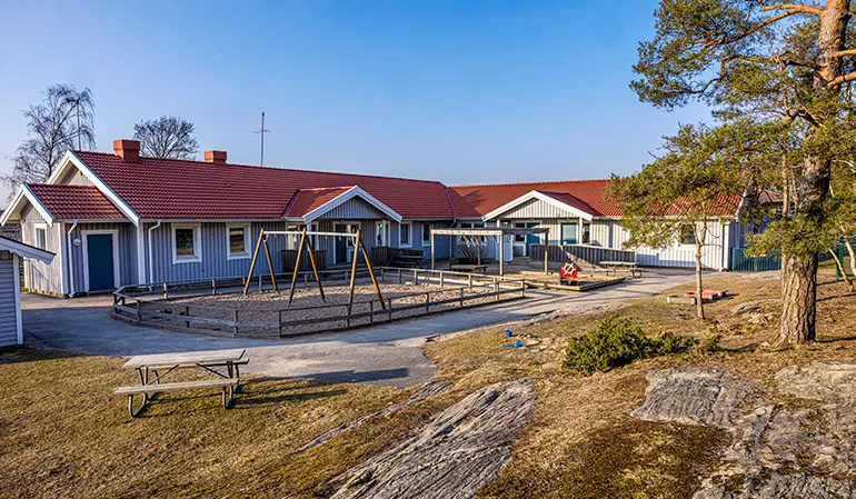 Förskolans blåa byggnad. Framför byggnaden syns en gård med gungor och träd.