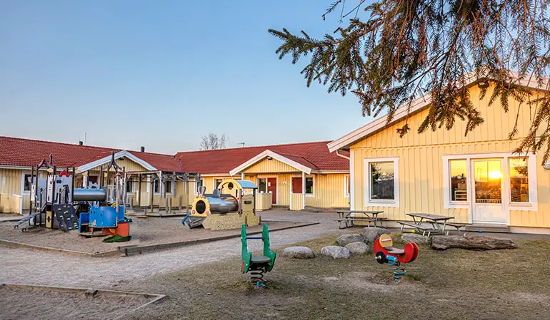 Håkansgårdens gula förskolebyggnad. Framför byggnaden finns en gård med flera klätterställningar och gunghästar.