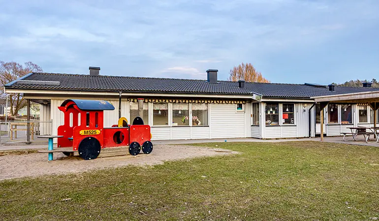 Särö förskolas vita byggnad. Framför byggnaden är förskolan gård med gräsmatta och sandlåda.