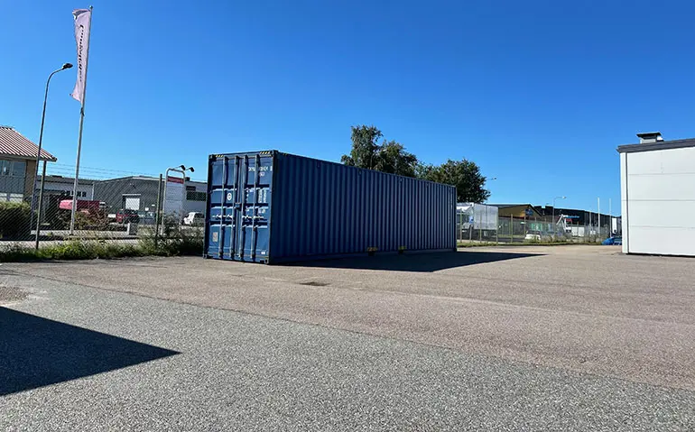 Blå container står på asfalterad parkeringsplats