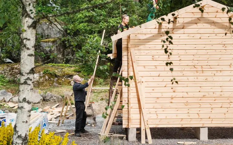 En man lyfter upp material till ett Attefalls hus i trä som håller på att byggas